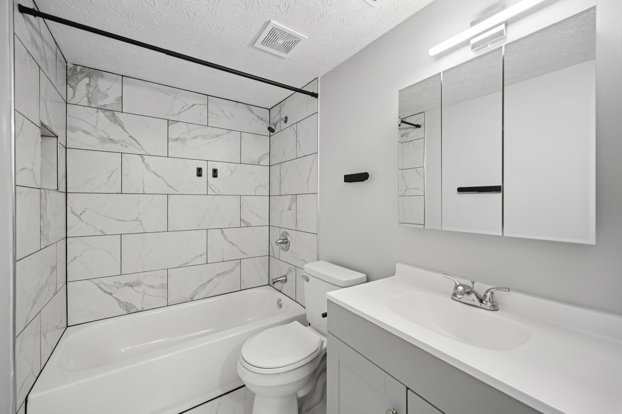 Newly renovated bathroom with marble-look tile, soaking tub, and modern vanity at Morse Creek Apartments